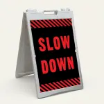 Slow Down sign with red text on black background and diagonal red and black hazard stripes
