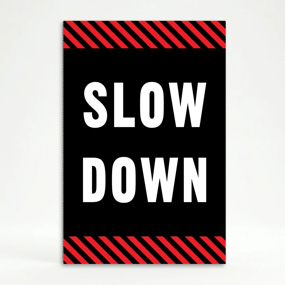 Slow Down sign with white text on black background and diagonal red and black hazard stripes