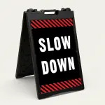 Slow Down sign with white text on black background and diagonal red and black hazard stripes
