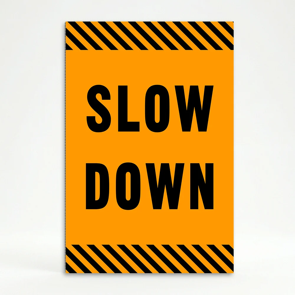 Slow Down sign with black text on orange background and diagonal black and orange hazard stripes