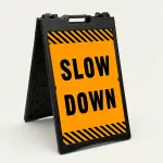 Slow Down sign with black text on orange background and diagonal black and orange hazard stripes