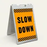 Slow Down sign with black text on orange background and diagonal black and orange hazard stripes
