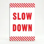 Slow Down sign with red text on white background and diagonal red and white hazard stripes