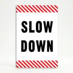 Slow Down sign with black text on white background and diagonal red and white hazard stripes