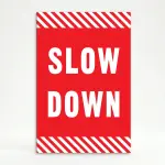 Slow Down sign with white text on red background and diagonal red and white hazard stripes