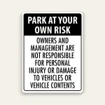 Black and white portrait sign with black header reading PARK AT YOUR OWN RISK above black text stating owners and management are not responsible for personal injury or damage to vehicles or vehicle contents.